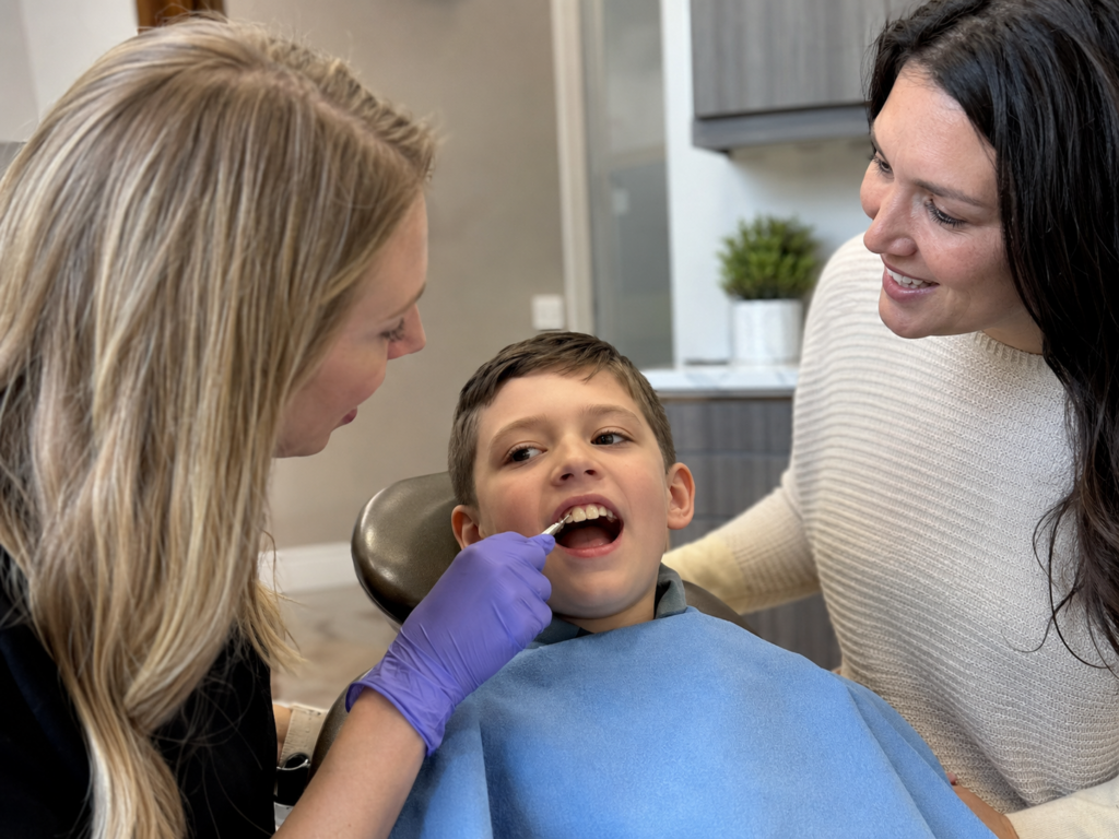 Pediatric dentist showing a parent the color difference between a child’s permanent teeth and baby teeth.